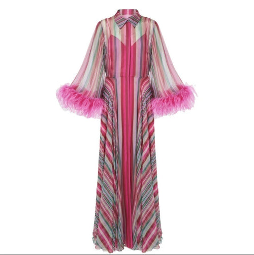 A long-sleeved maxi dress with vertical pink, red, and gray stripes, featuring a high collar and voluminous pink feathered cuffs, shown against a plain white background.
