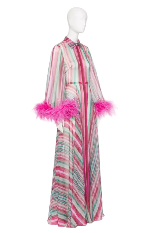 A long-sleeved maxi dress with vertical pink, green, and white stripes, featuring bright pink feather trim at the cuffs, displayed on a white mannequin against a white background.