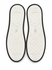 Top-down view of a pair of white slip-on shoes showing the textured outsoles with black trim, on a white background.