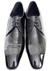A pair of men's black leather dress shoes with a glossy finish, featuring a classic oxford style with a closed lacing system and a pointed toe, displayed on a dark gray background.