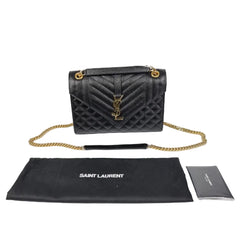 Black quilted handbag with gold chain and Saint Laurent pouch on a white background