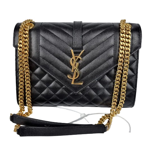 Black quilted handbag with gold chain strap on a gray background