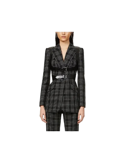 A model wearing a black and white plaid blazer with structured shoulders and a matching black belt with a silver buckle, paired with matching plaid trousers, set against a plain white background.
