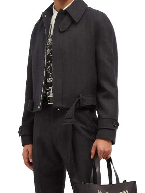 A man wearing a black denim jacket, black shirt, and black trousers, holding a black leather bag.