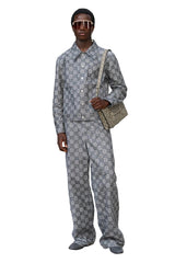 Man wearing a patterned suit with sunglasses and a bag on a white background