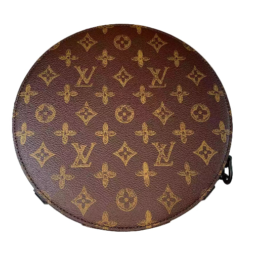 Round brown leather bag with gold monogram pattern on a marble surface
