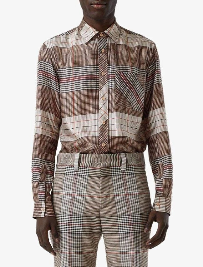 A model wearing a long-sleeve button-up shirt and matching trousers in a brown, beige, and red plaid pattern, photographed against a light gray studio background.