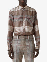 A model wearing a long-sleeve button-up shirt and matching trousers in a brown, beige, and red plaid pattern, photographed against a light gray studio background.