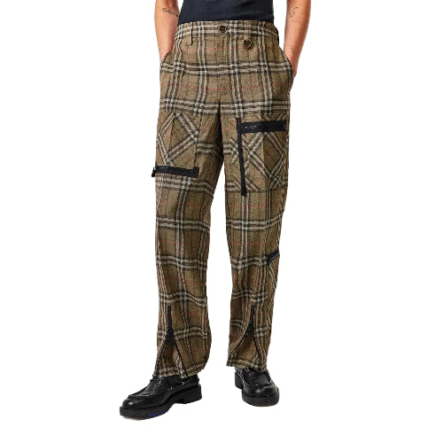 A person wearing loose-fit plaid trousers in brown, beige, and black, with black cargo-style pockets and black shoes, photographed against a light gray studio background.