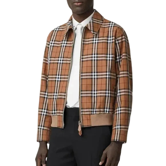 A man wearing a brown and beige plaid overshirt with a white shirt and black trousers, shown against a plain white background.