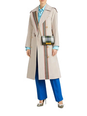 A model wearing a beige double-breasted trench coat with vertical plaid stripes, styled with a light blue shirt, blue trousers, and a small plaid shoulder bag, against a light gray studio background.