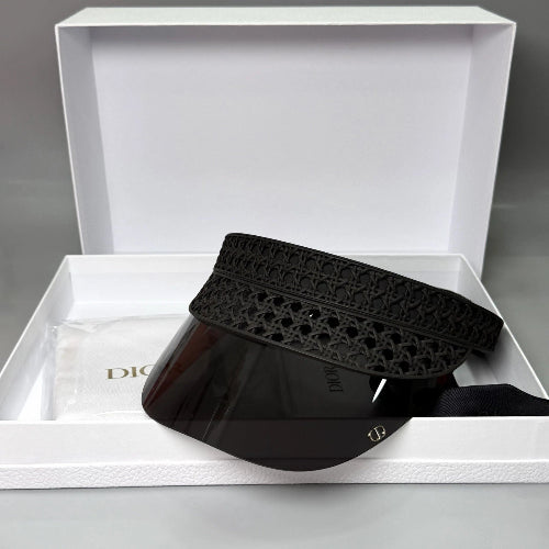 A black Dior visor with a patterned fabric headband and a clear shield lens, presented inside an open white Dior gift box with a dust bag.