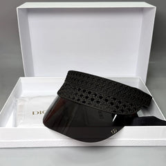 A black Dior visor with a patterned fabric headband and a clear shield lens, presented inside an open white Dior gift box with a dust bag.