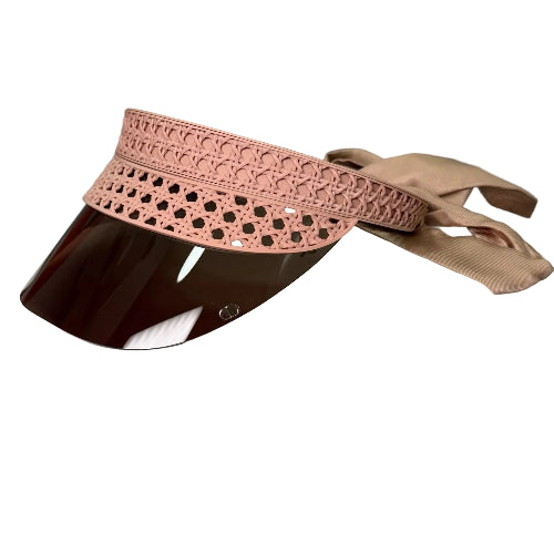 A pink visor with a decorative cutout pattern on the crown and a glossy dark brown visor, displayed on a white box with a beige ribbon against a gray background.
