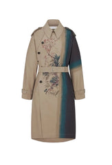 A beige trench coat with a vertical color-blocked panel in dark navy and teal, featuring a floral print on the front and a matching belt, shown against a light gray background.