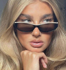 A close-up of a woman wearing dark rectangular sunglasses with a thin silver metal frame and a thick black lower rim.