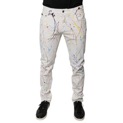 White slim-fit jeans with a colorful paint splatter print, shown on a model from the waist down wearing black sneakers against a white background.