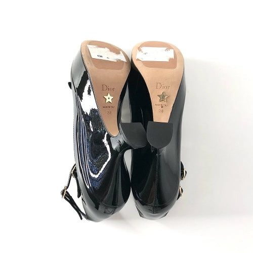 A pair of black patent leather Christian Dior high heels shown from the back, featuring a beige insole with a gold star logo and size markings, on a white background.