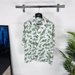 Floral patterned shirt on a hanger against a white wall with a plant in the corner.