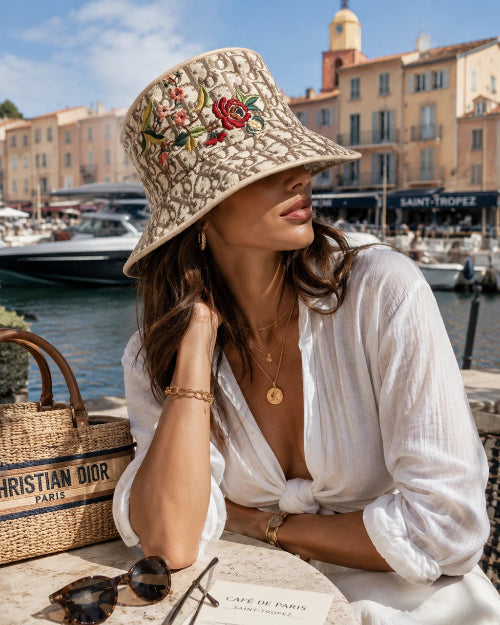 Woman wearing a floral embroidered hat in a scenic location with boats and buildings.