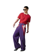 A model wearing a red short-sleeve knit polo shirt and purple wide-leg trousers with red and white graphic details, standing against a light gray studio backdrop with a green floor.
