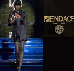 Model on a runway wearing a black outfit with a high collar, holding a product, with 'FENDACE' branding.
