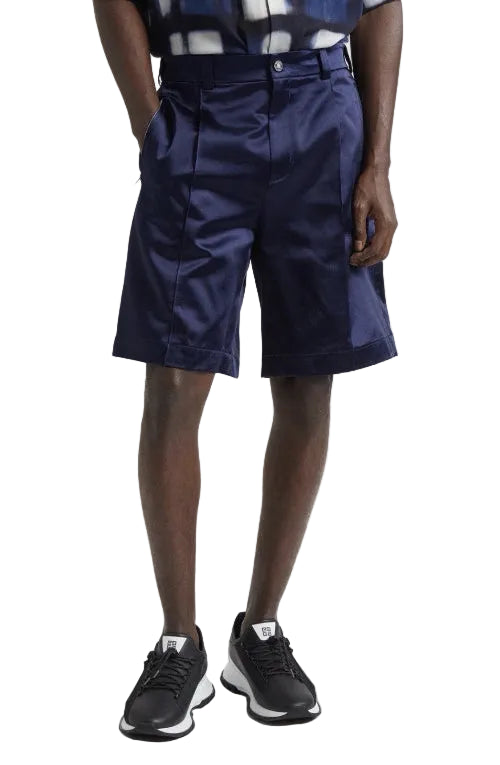 Person wearing navy shorts with a belt and black shoes on a plain background