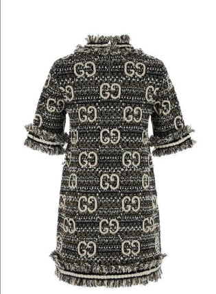 A Gucci tweed mini dress with an allover black and beige GG monogram pattern and fringed trim, shown against a plain white background.
