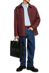 A man wearing a red and black patterned overshirt, blue jeans, and black shoes, holding a black briefcase against a plain white background.