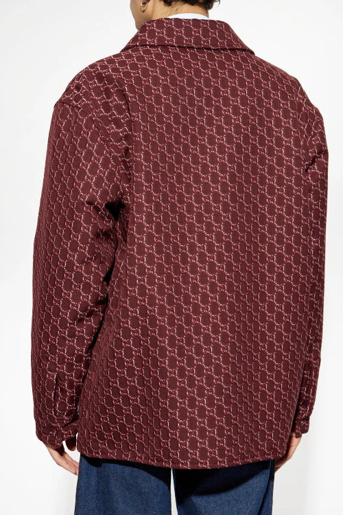 A close-up of a person wearing a dark red button-up shirt with a textured, patterned weave and blue jeans.