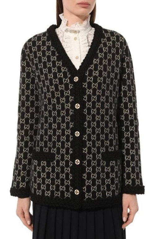 A close-up of a person wearing a black cardigan with a white geometric pattern, paired with a white ruffled collar and a dark skirt.