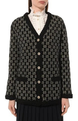 A close-up of a person wearing a black cardigan with a white geometric pattern, paired with a white ruffled collar and a dark skirt.