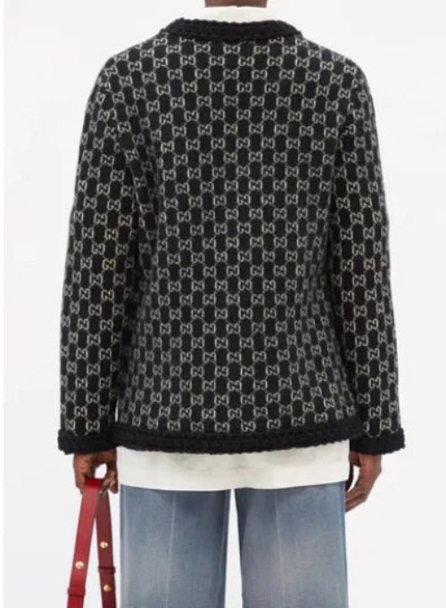 A black knit cardigan featuring an all-over white interlocking monogram pattern, shown from the back on a model wearing blue jeans and a white shirt.