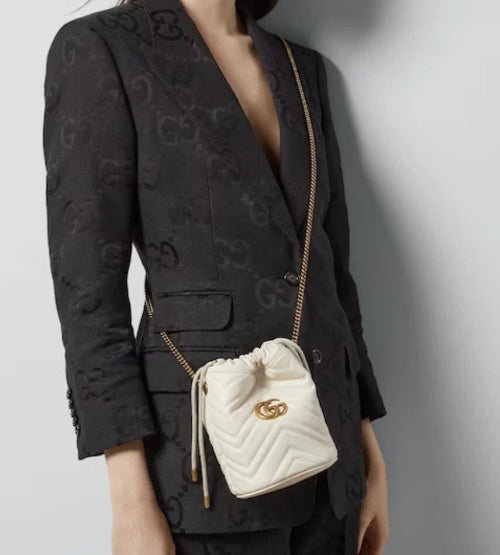 Person wearing a black patterned blazer with a white Gucci handbag.