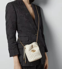 Person wearing a black patterned blazer with a white Gucci handbag.