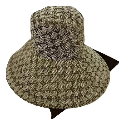 A Gucci sun hat featuring the brand's signature GG monogram canvas in beige and brown, displayed on a dark brown surface against a white background.