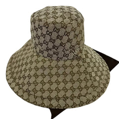 A Gucci sun hat featuring the brand's signature GG monogram canvas in beige and brown, displayed on a dark brown surface against a white background.