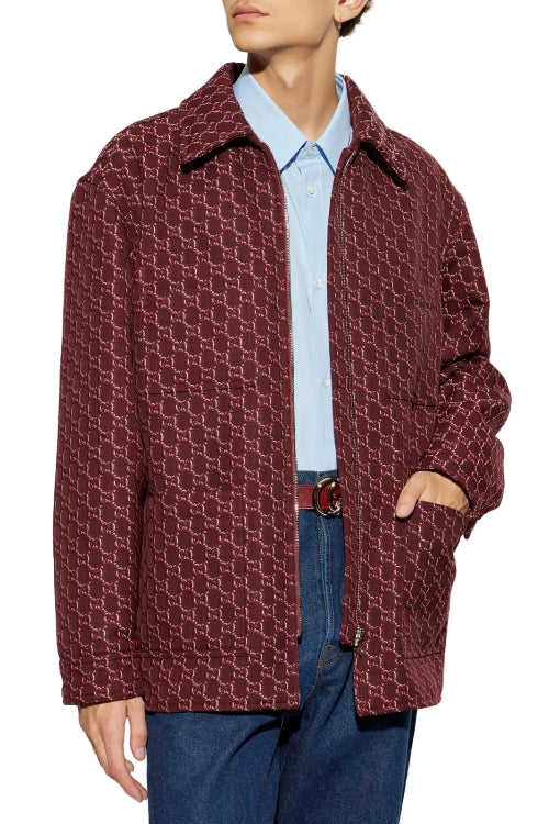 A man wearing a burgundy textured overshirt over a light blue collared shirt and blue jeans, shown from the chest down against a plain white background.