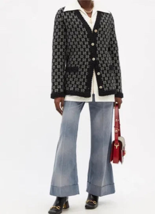 A model wearing a black and white patterned button-up shirt, light-wash wide-leg jeans, and a red handbag, shown in a cropped studio fashion shot.