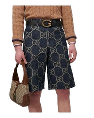 Person wearing Gucci patterned shorts and holding a matching handbag on a white background