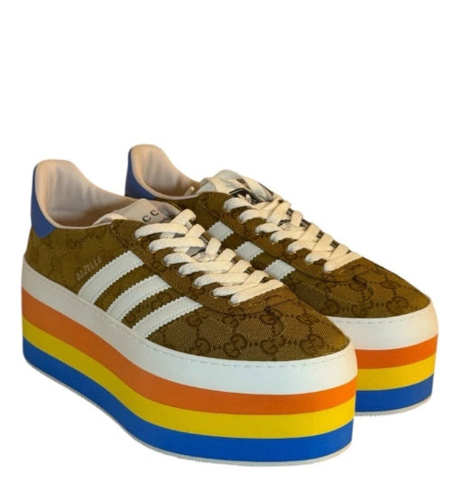 A pair of low-top platform sneakers featuring a brown and gold patterned upper, cream laces, and a thick platform sole with rainbow stripes.