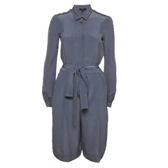 A slate blue long-sleeve jumpsuit with a collar, button front, shoulder epaulets, and a matching fabric tie belt at the waist, shown against a light gray background.