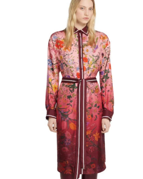 A woman modeling a long red patterned coat with a matching belt, shown against a plain white studio background.