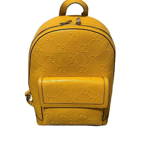 Yellow backpack with a prominent brand logo on a black surface against a beige wall.