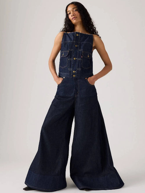 Person wearing a dark denim sleeveless jacket and wide-leg jeans on a white background