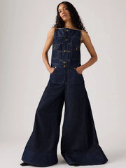 Person wearing a dark denim sleeveless jacket and wide-leg jeans on a white background