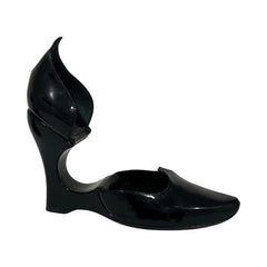 A single black patent leather wedge heel shoe with a unique sculptural, flame-like heel and open side cutout, shown against a plain white background.