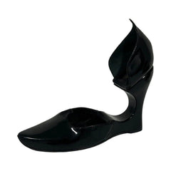 A single black patent leather wedge pump with a pointed toe and a sculptural, curved heel, shown against a plain white background.