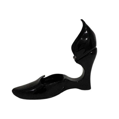 A single black patent leather wedge shoe with a unique sculptural heel and pointed toe, shown against a plain white background.