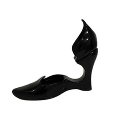 A single black patent leather wedge shoe with a unique sculptural heel and pointed toe, shown against a plain white background.